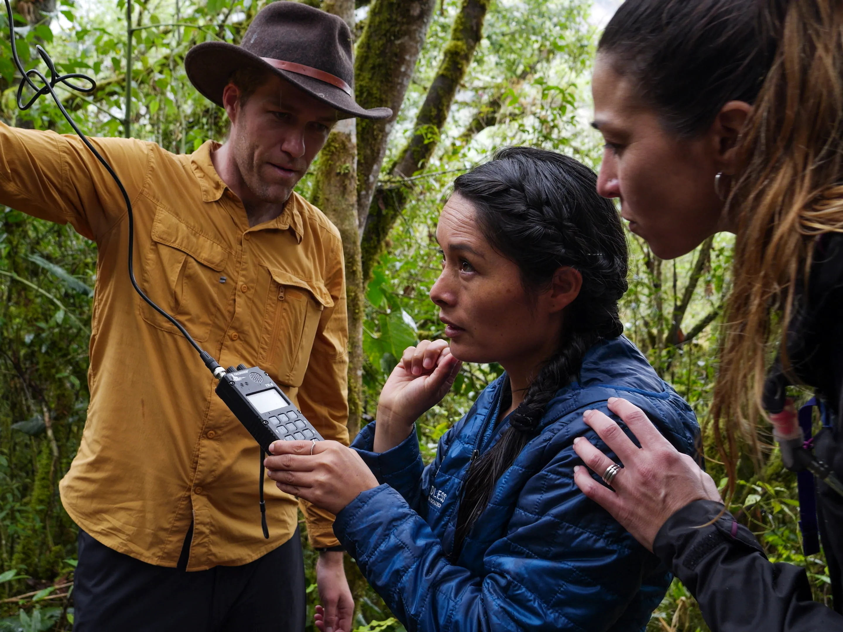 A group of people sitting on a log at the edge of a river, pointing into the distance