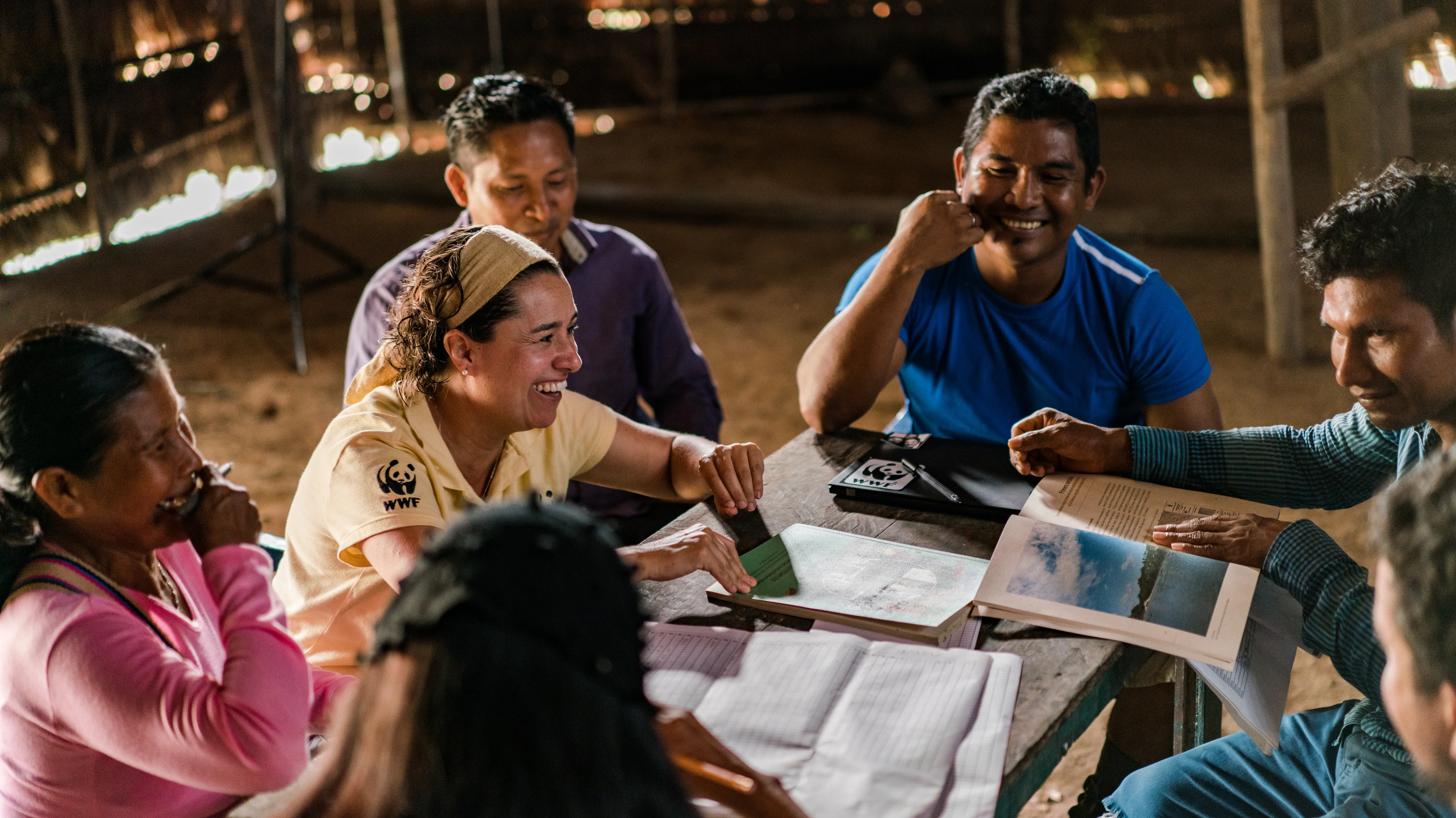 A group of people laughing and smiling around a table full of books and papers