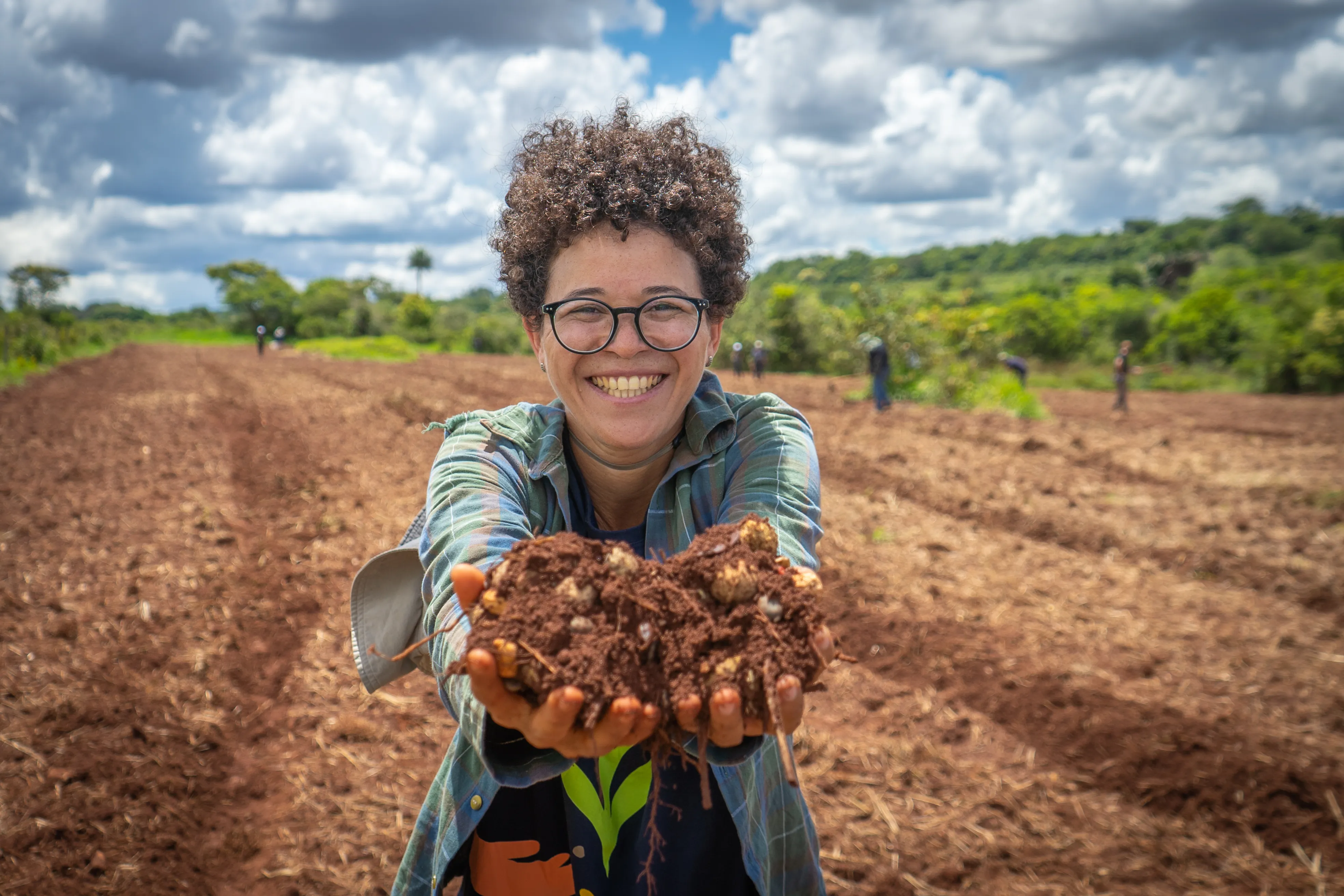 A woman smiling in a field of crops with soil in her outstretched hands